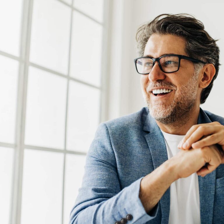 Business man looking outside the window in an office. Senior business man thinking about work while sitting at his desk in a suit.