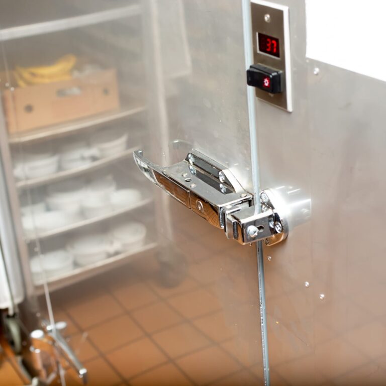 A view of a door handle that leads to a walk-in fridge inside a restaurant kitchen.