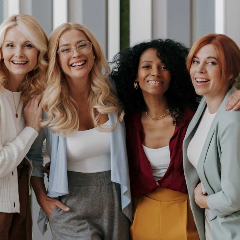 Multi-ethnic group of happy mature women bonding while standing in office together